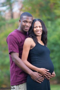 Happy expecting couple. Man standing behind woman with both their hands on her belly.