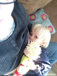 child is looking up at the camera while holding a doll and nursing