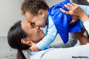 Mother holding toddler above her head, faces together, smiling
