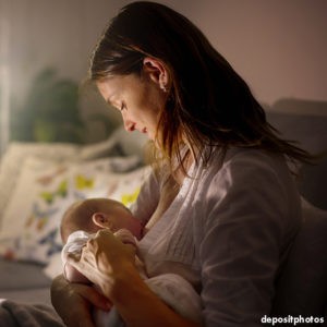 Woman is holding, looking down, and smiling at the nursing baby.