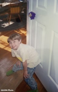 Kate at five years old, standing in front of a door, smiling