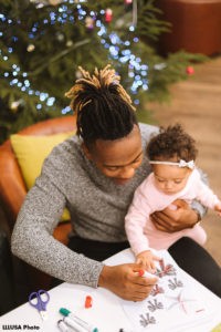 Dad drawing with his toddler daughter on his lap, in front of christmas tree