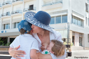 Mother breastfeeding baby while hugging older child
