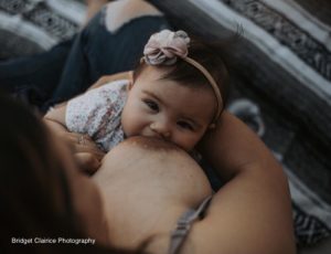 Baby looking at camera, smiling, while nursing