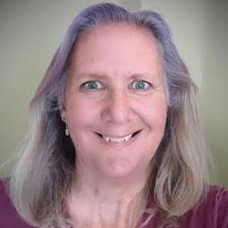 White person with long hair and smile, teeth showing, is looking at the camera.